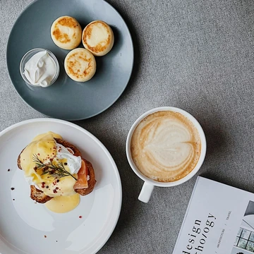 A plate of eggs benedict, pancakes, and a latte